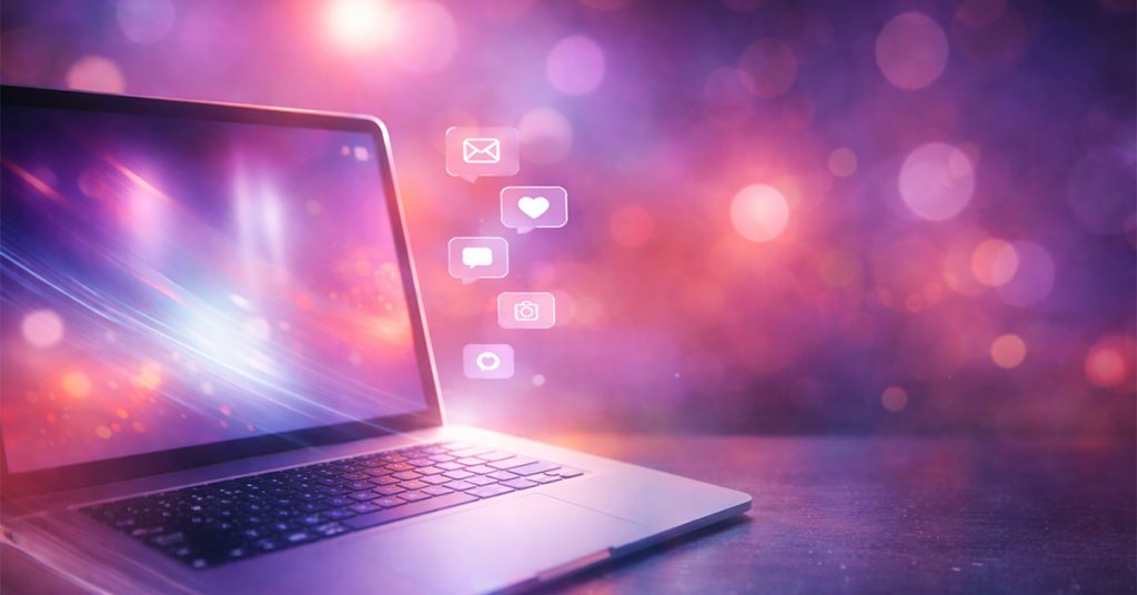 a colorful illustration of a laptop on a table with abstract lights and social media icons in the background