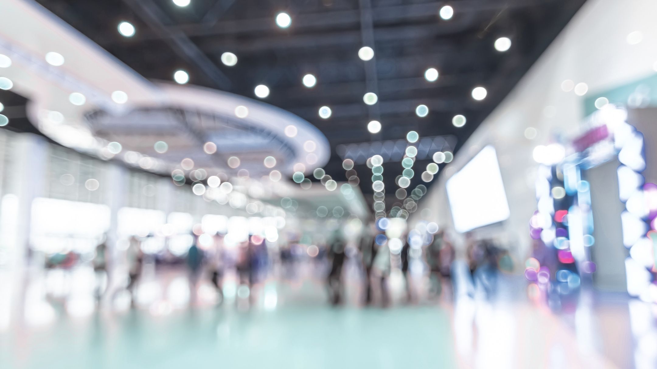 A soft focus photograph of an upscale trade show floor with attendees in the distance